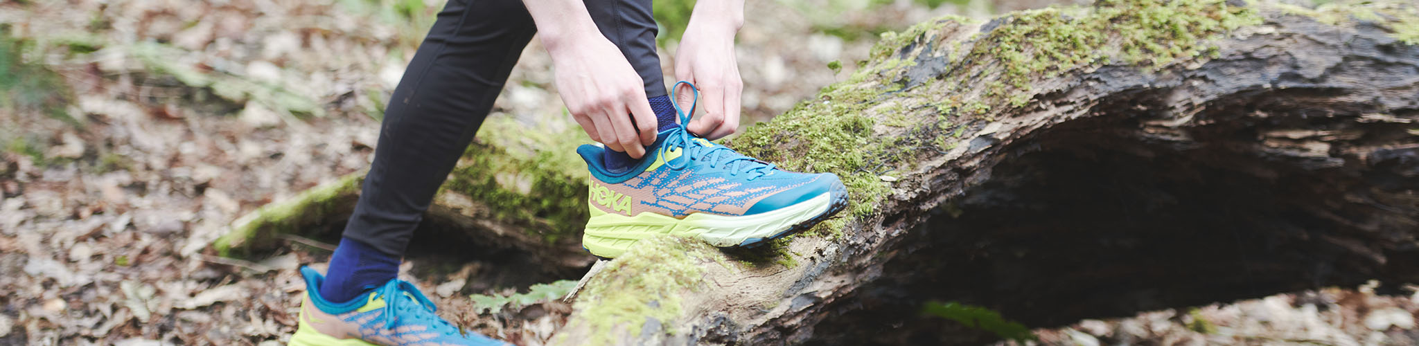 Men's hands are tieing shoe laces on a Hoka running shoe somewhere outdoors.