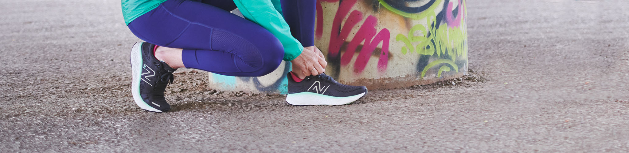 Woman's hands are tieing shoe laces on a New Balance running shoe somewhere outdoors.