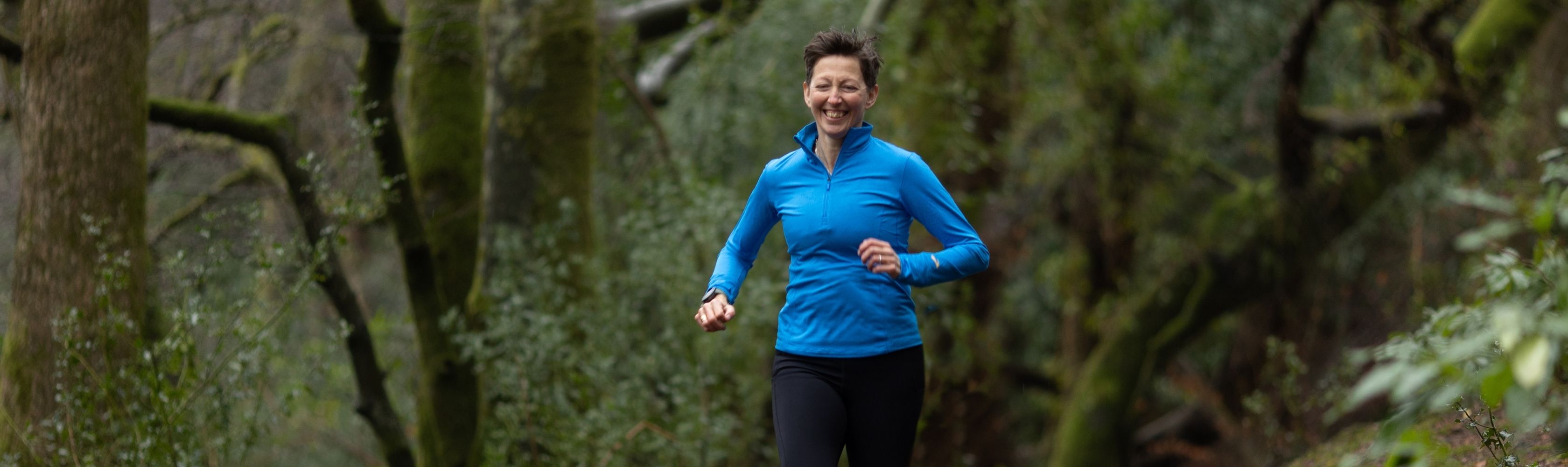 A lady running in the forest wearing a bright blue running top