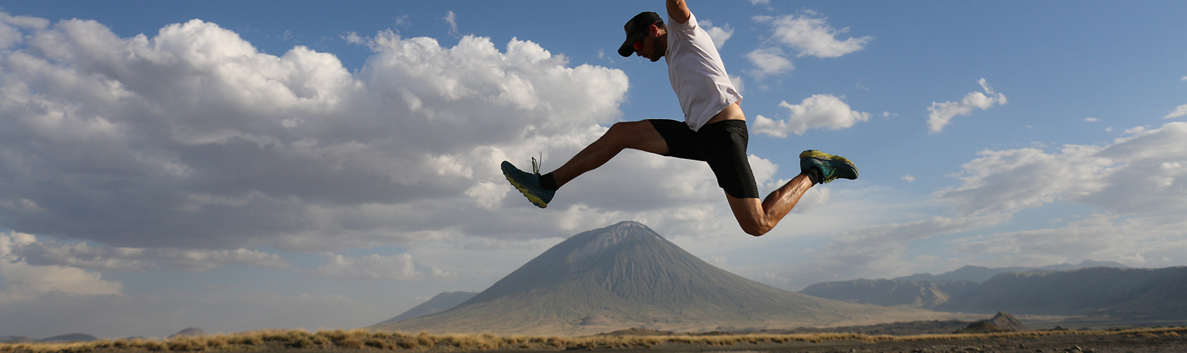 A man jumpes in a shite t-shirt and shorts over a mountain in the background