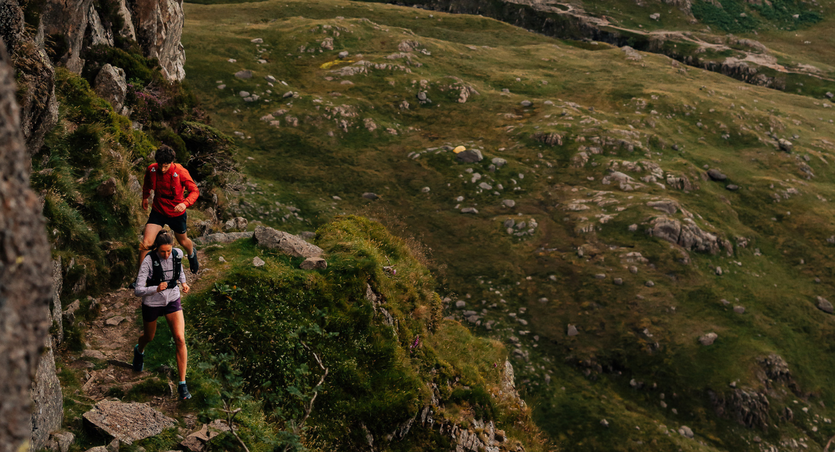 And a man and woman run in the mountains together up a trail in the sun