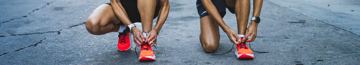 Two individuals look down and tie up their bright orange running trainers ready to race.