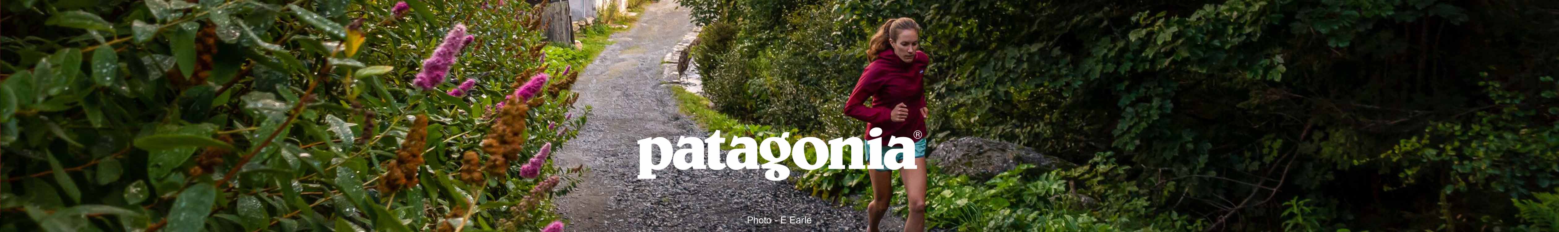 A woman is running on a country lane, wearing summer Patagonia clothing and runnish shoes.