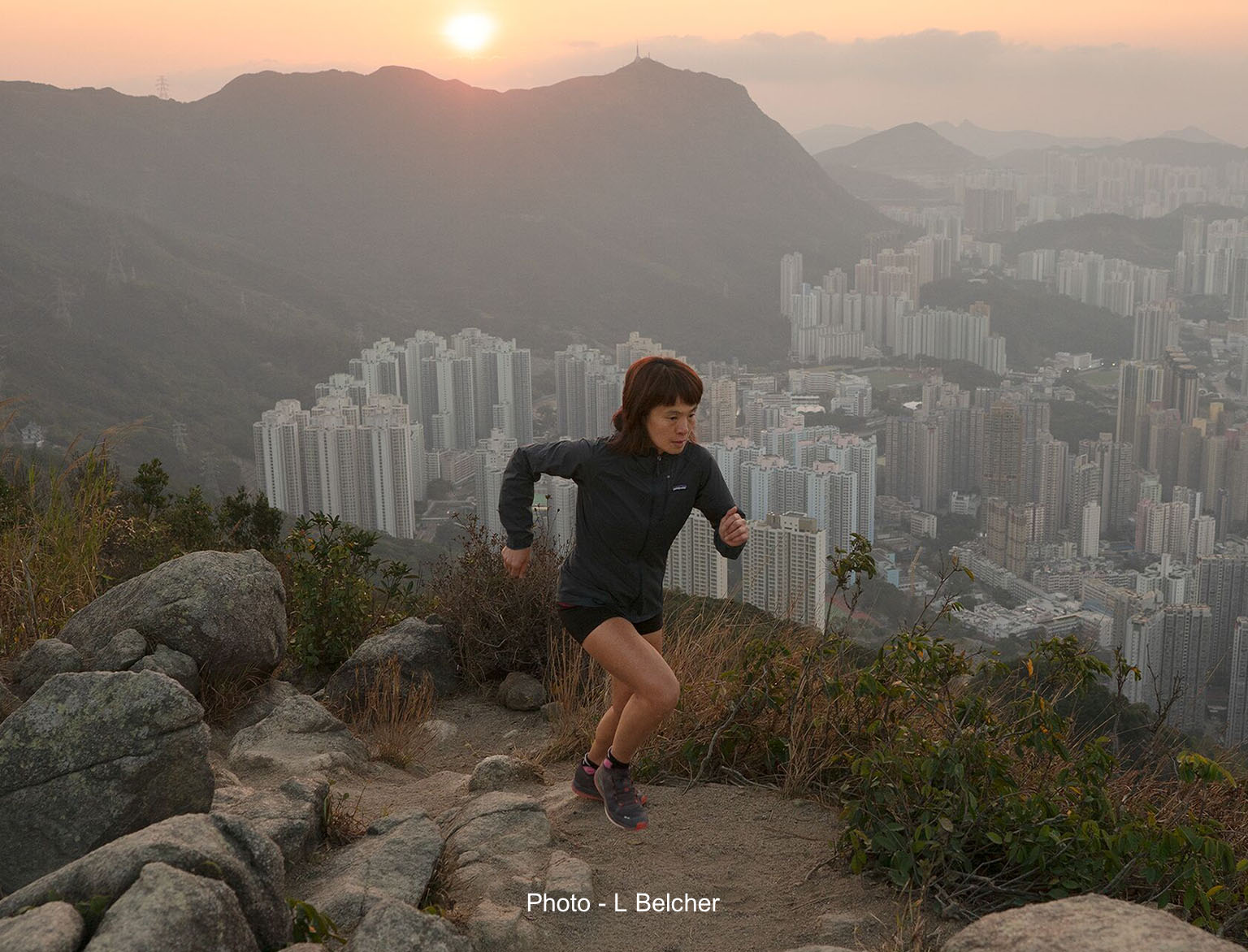 A person is running on a trail, wearing running shoes and Patagonia shorts and light jacket.