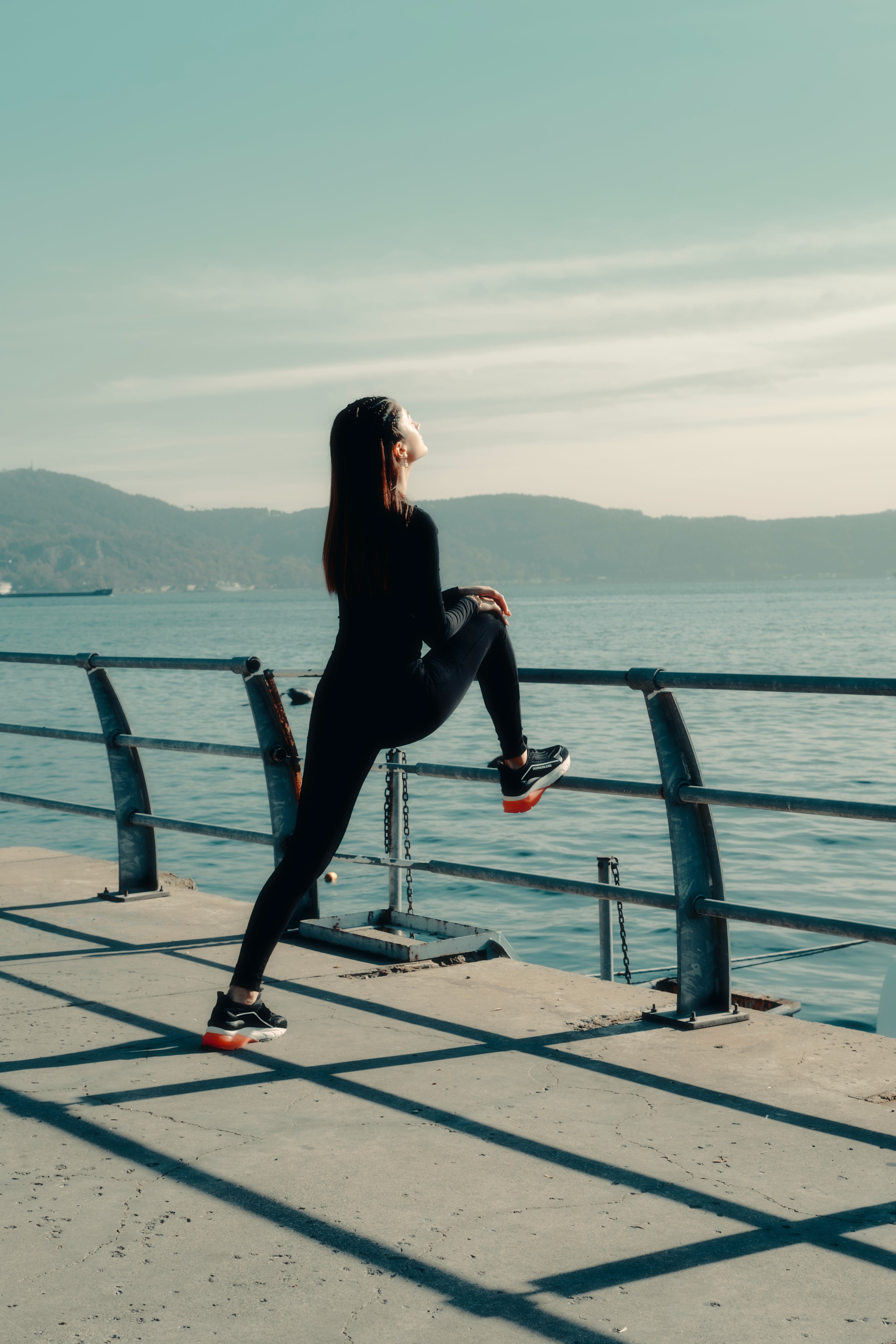 An image of a woman by the sea, stretching in her running gear and running shoes