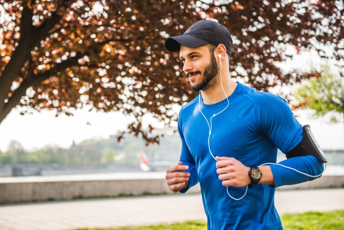 A man on a run wearing a running cap with his earphones in 