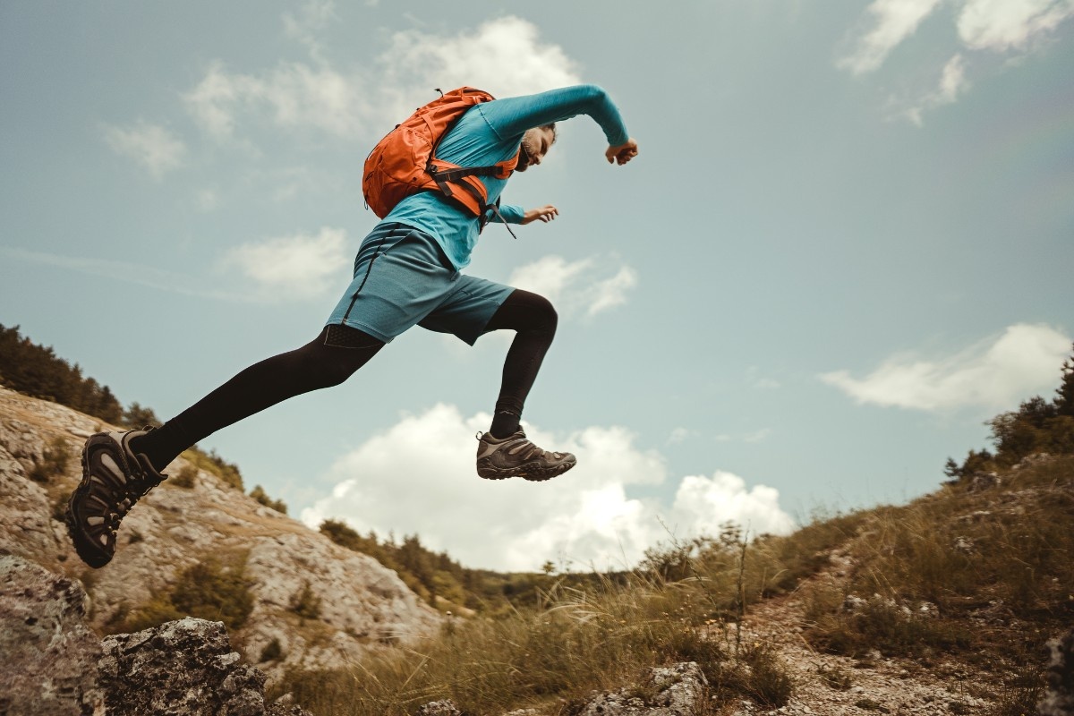 A man taking a leap across a trail with a running pack on 