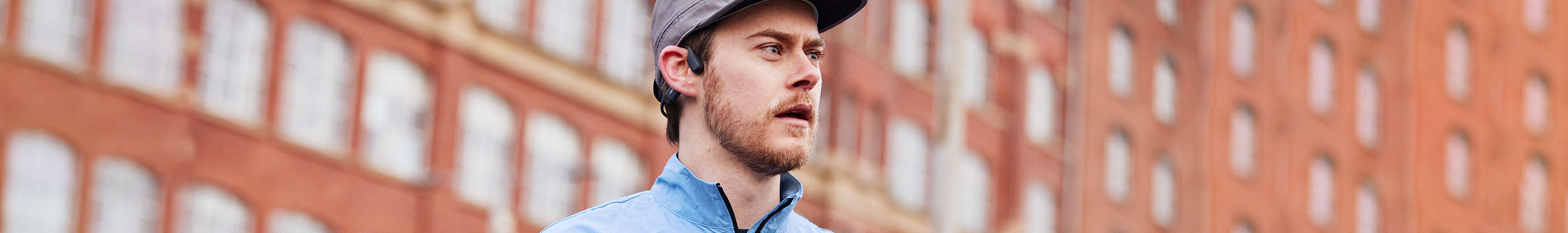 Running headphones. A man in a blue jacket wearing a hat and a pair of Shokz headphones