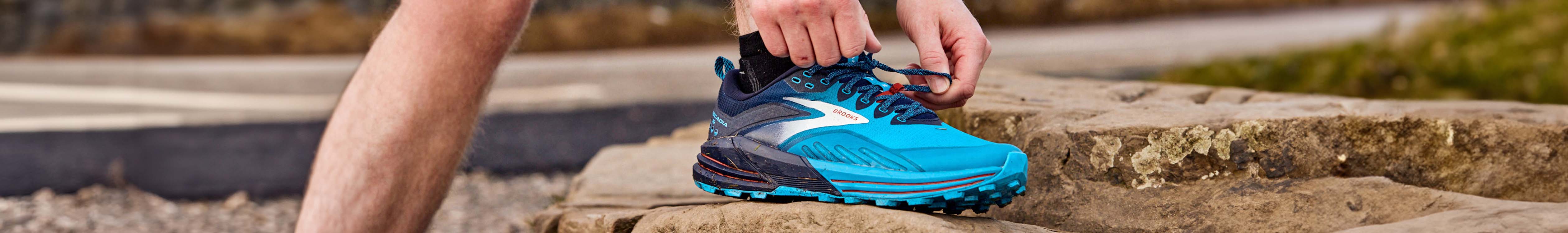 Shop men's trail running shoes. A runner tieing up his laces