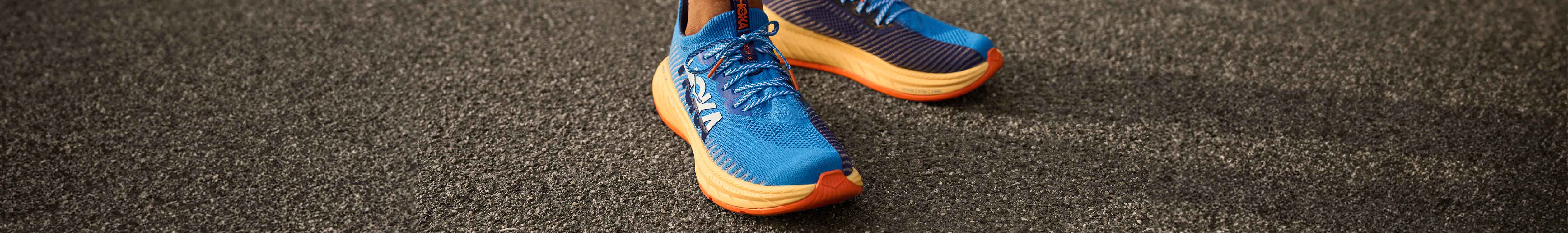 Shop men's race and lightweight running shoes. A man in blue Hoka shoes