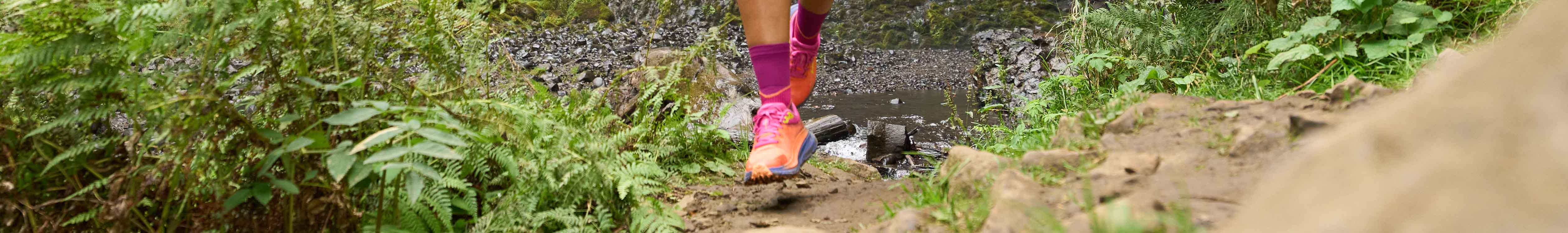 Shop women's trail running shoes. A woman running on a dirt path 