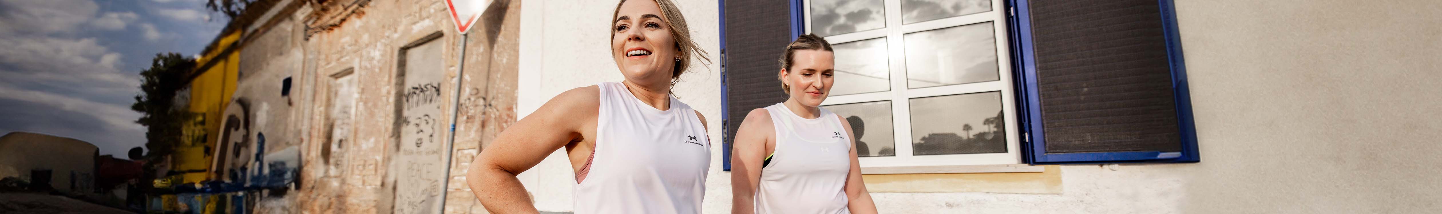 Shop women's running clothing. Two women in running clothes walking in an urban setting