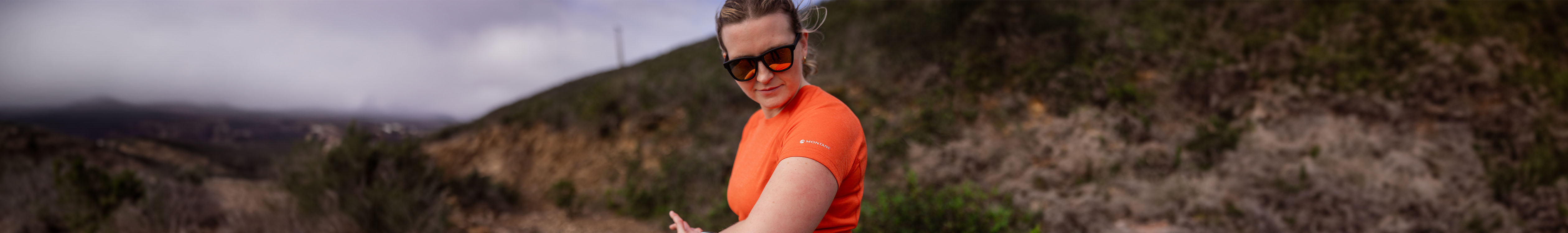 Shop sunglasses. A woman is in an orange t-shirt, wearing sunglasses