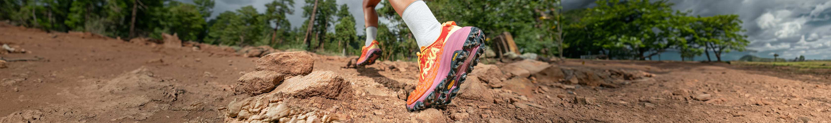 Shop Trail running shoes. A runner in Hoka running shoes on a trail