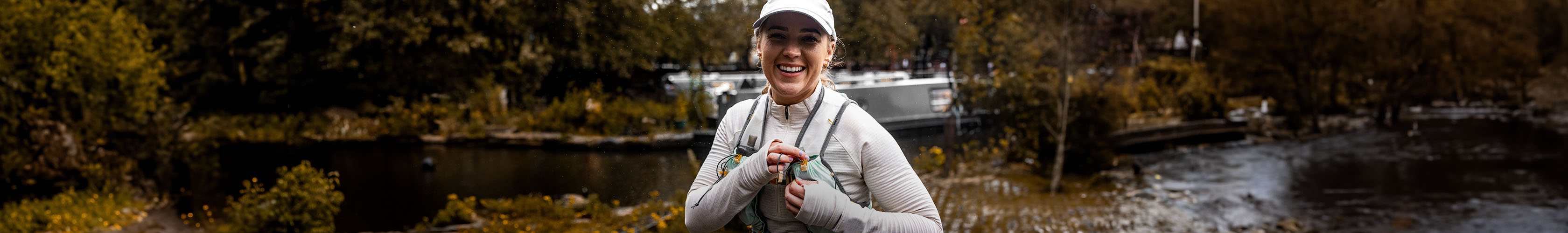 Shop trail running gear. A woman standing on a trail path next to a water canal