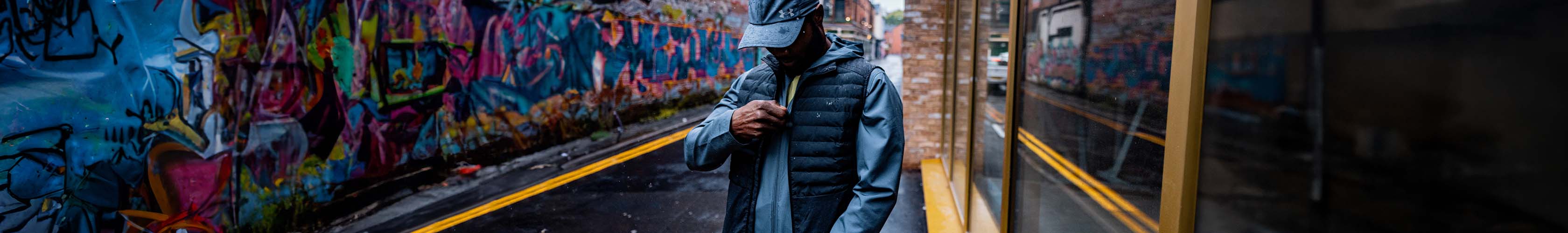 Shop new season running jackets and gilets. Man zipping up jacket.