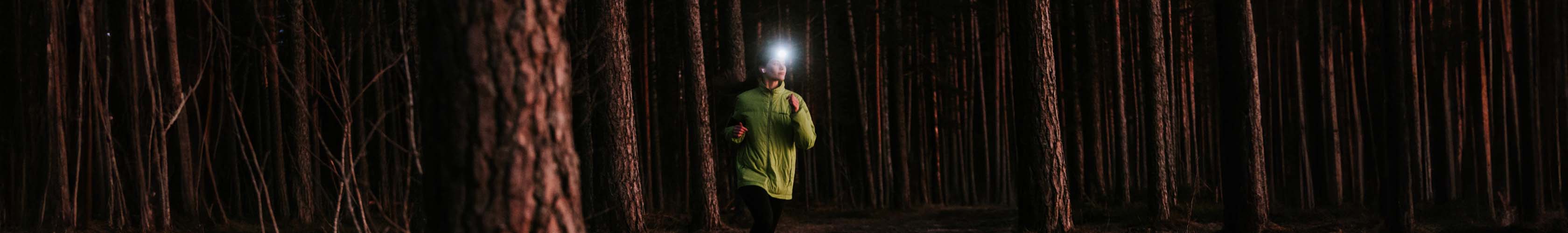 Shop hi-vis. A female runner wearing hi-vis jacket and headtorch running between the treas