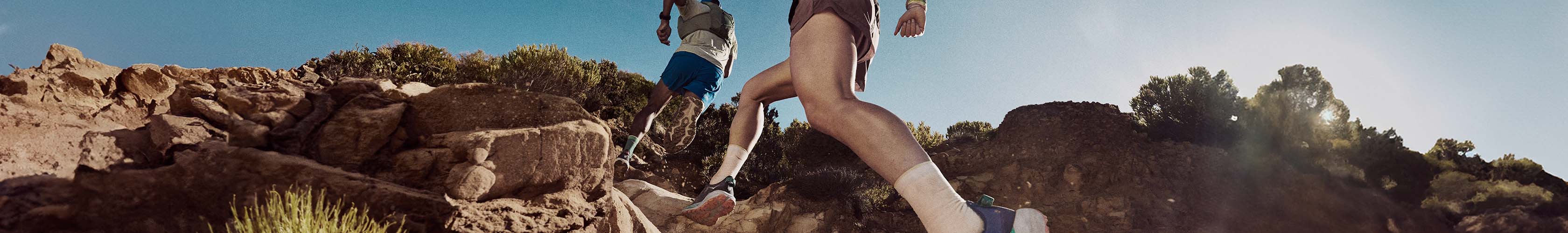 Shop trail running gear. Two runners running uphill on a trail path