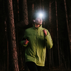 Shop hi-vis. A female runner wearing hi-vis jacket and headtorch running between the treas