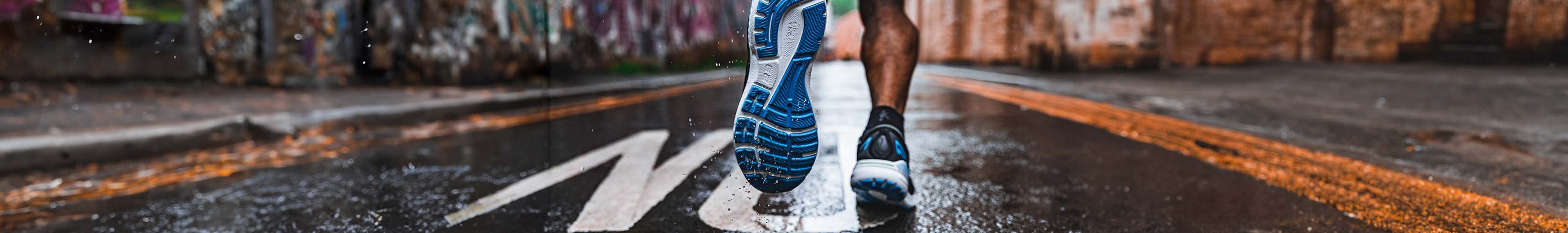 Shop road running shoes. A person running on a wet road