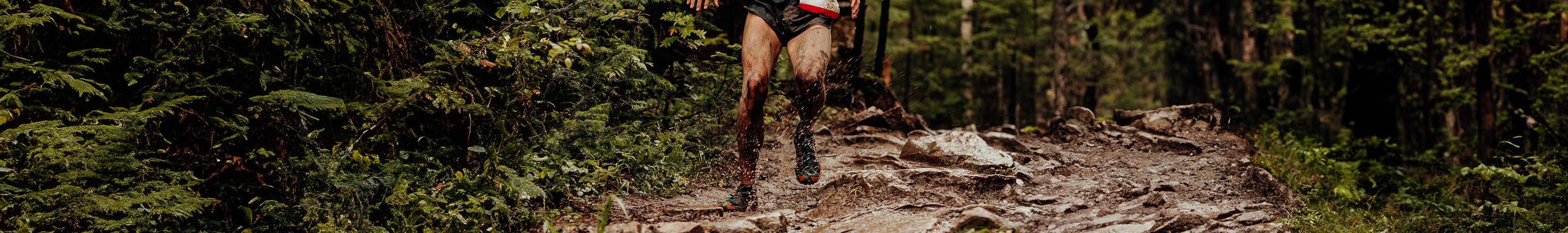 Shop trail running shoes. Person running through a muddy path