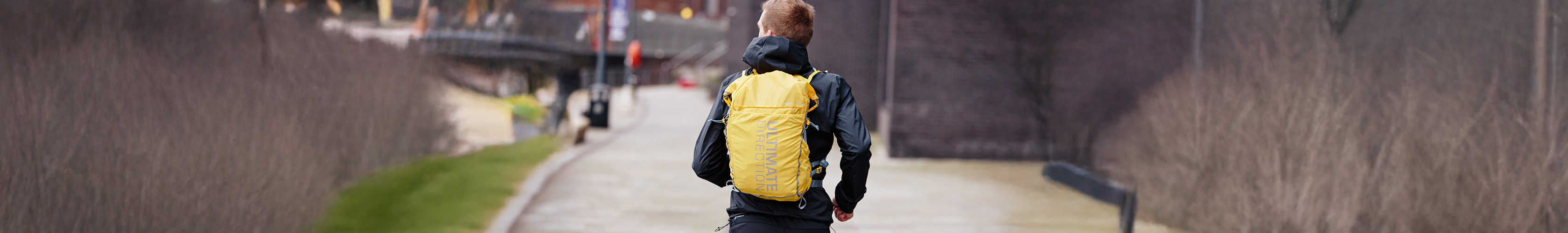 Shop backpacks. A man running wearing a yellow backpack