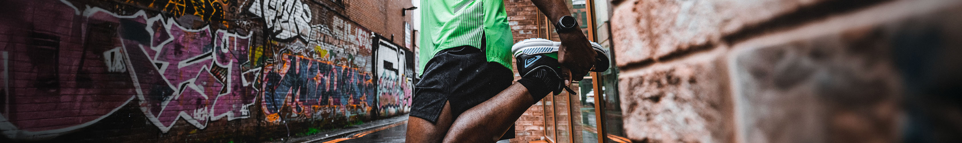 Shop Clothing. Man in green T-shirt and black shorts stretching before the run